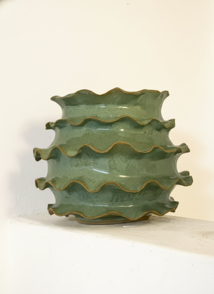 Green ceramic vase with wavy design on a white background